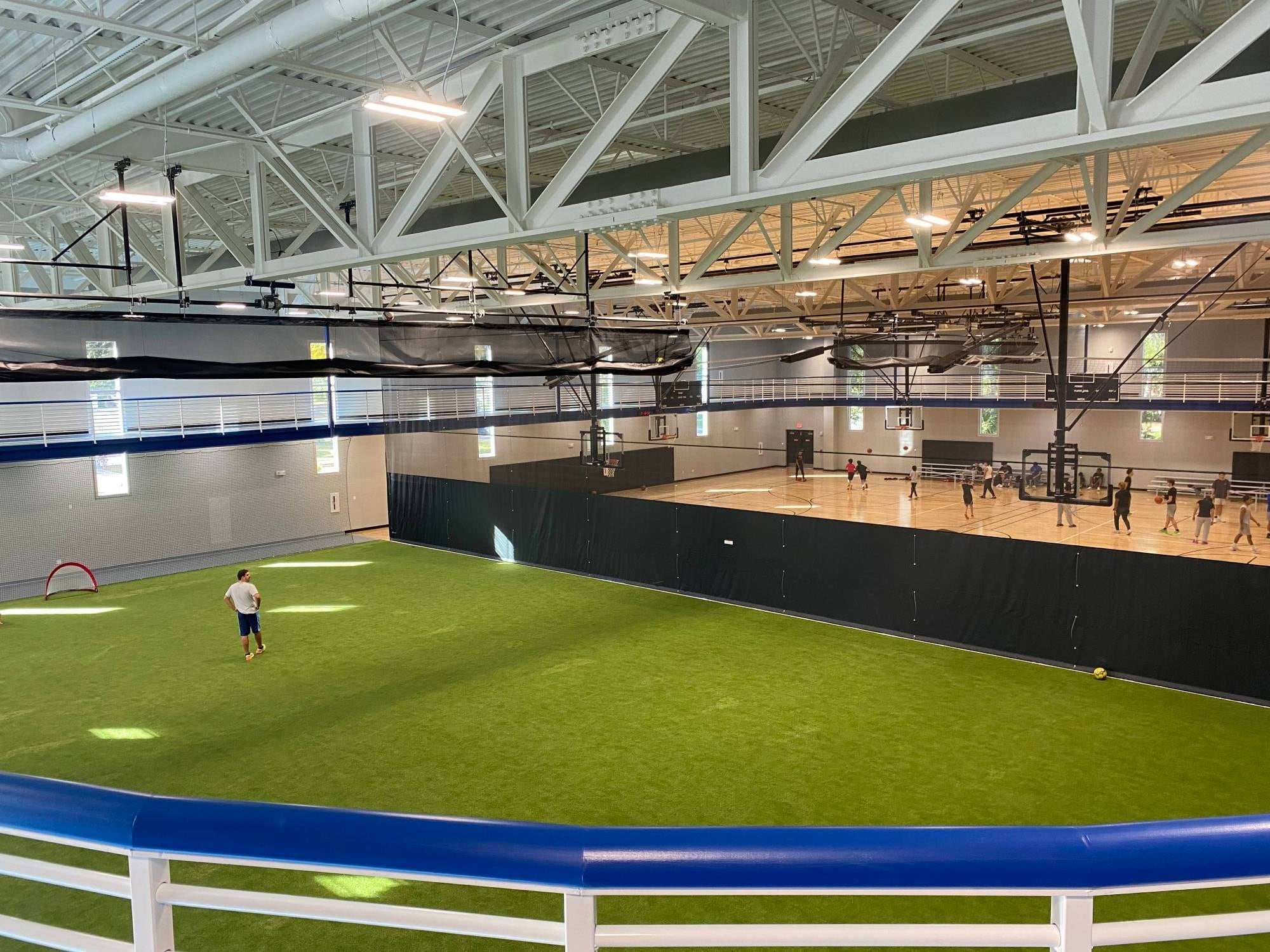 Indoor turf field beside basketball courts, separated by a floor-to-ceiling divider curtain