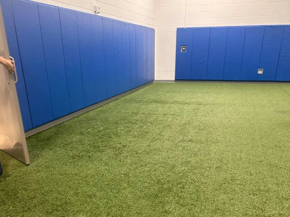 Blue padded wall pads lining a block wall above a green indoor turf floor
