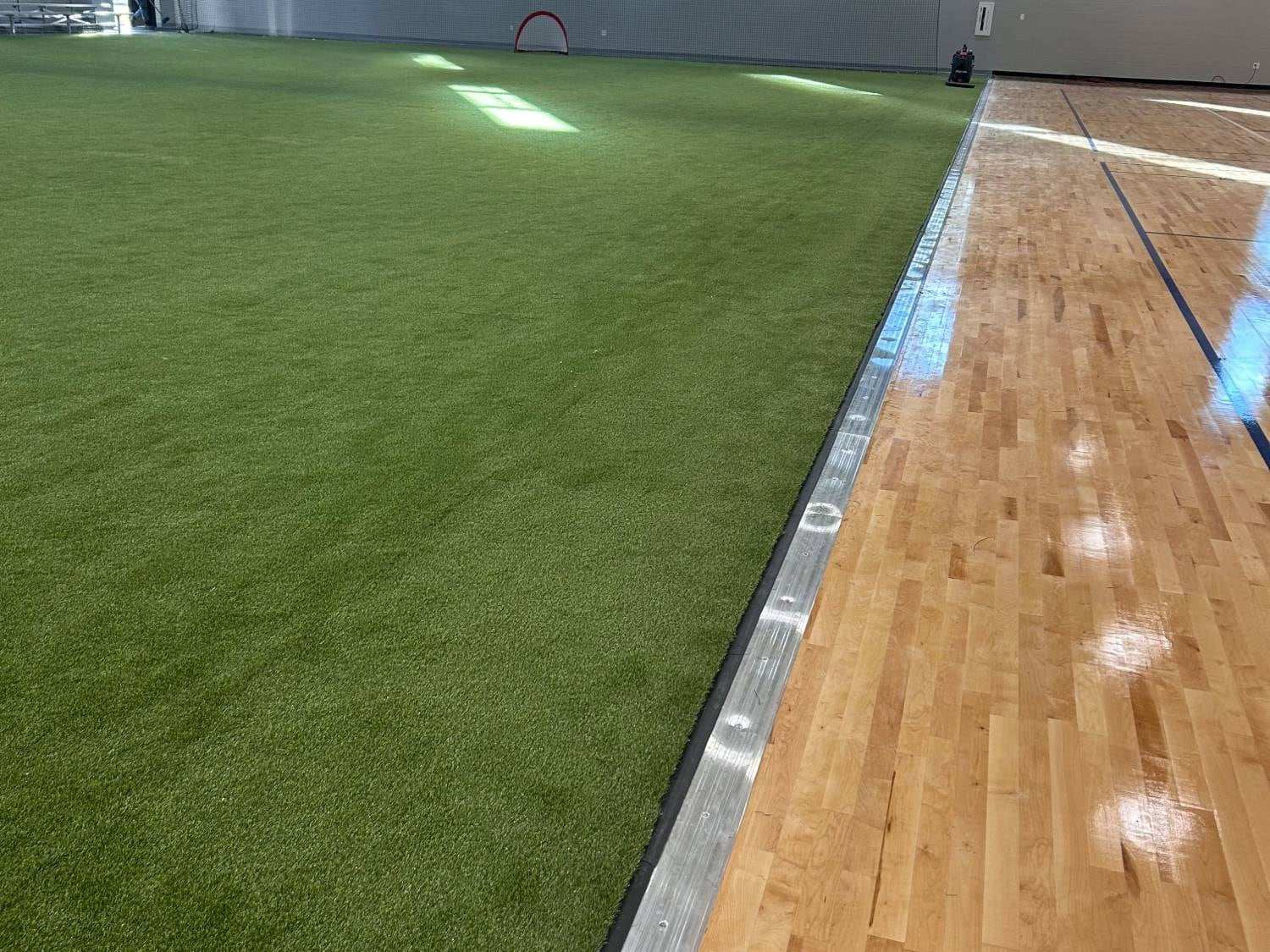 Metal transition strip where an indoor turf field meets a hardwood basketball court