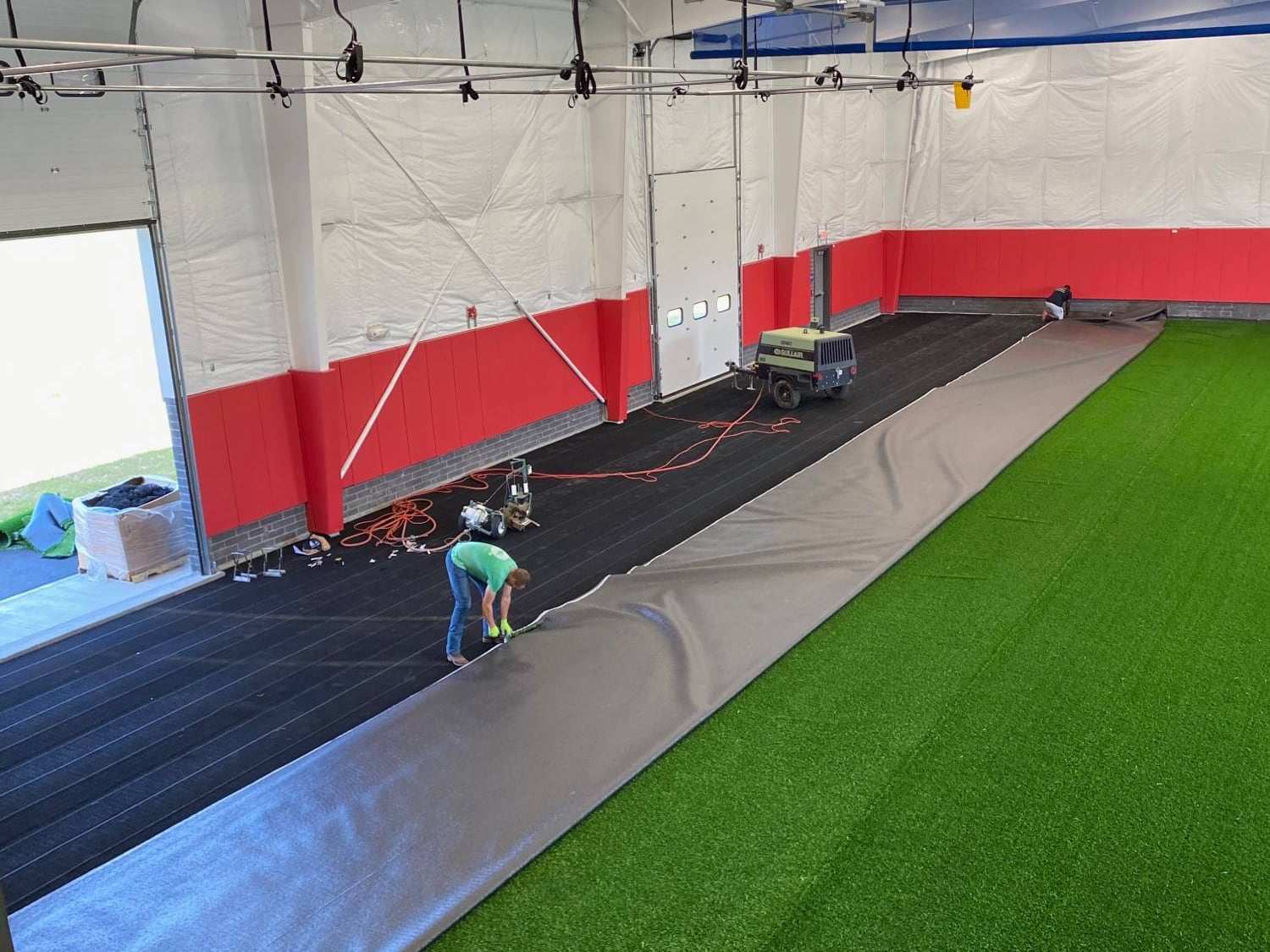 Installer laying foam pad and rolling out turf over the base layer inside a training facility