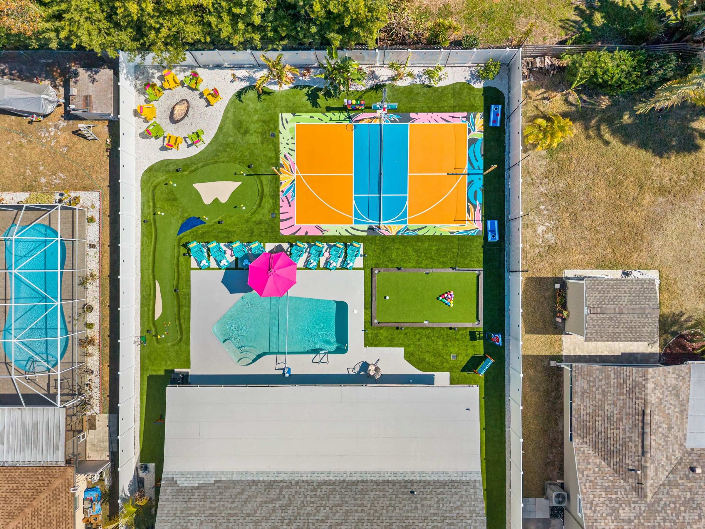 Aerial view of a backyard with turf around a pool, a pickleball court and a putting green