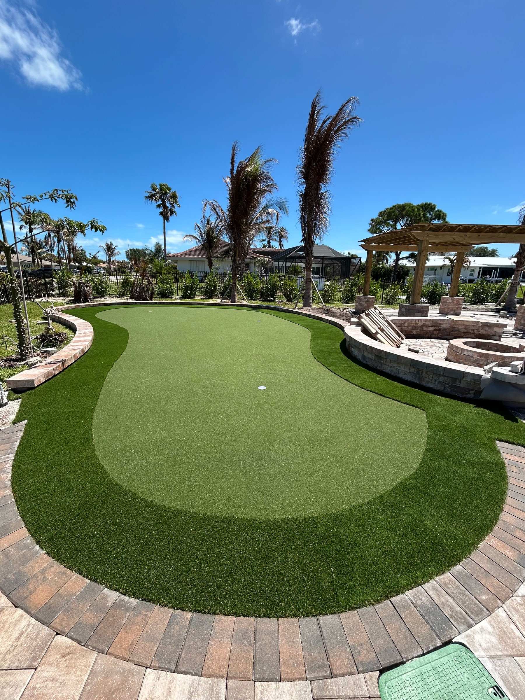 Kidney-shaped turf putting green edged with brick pavers and palms