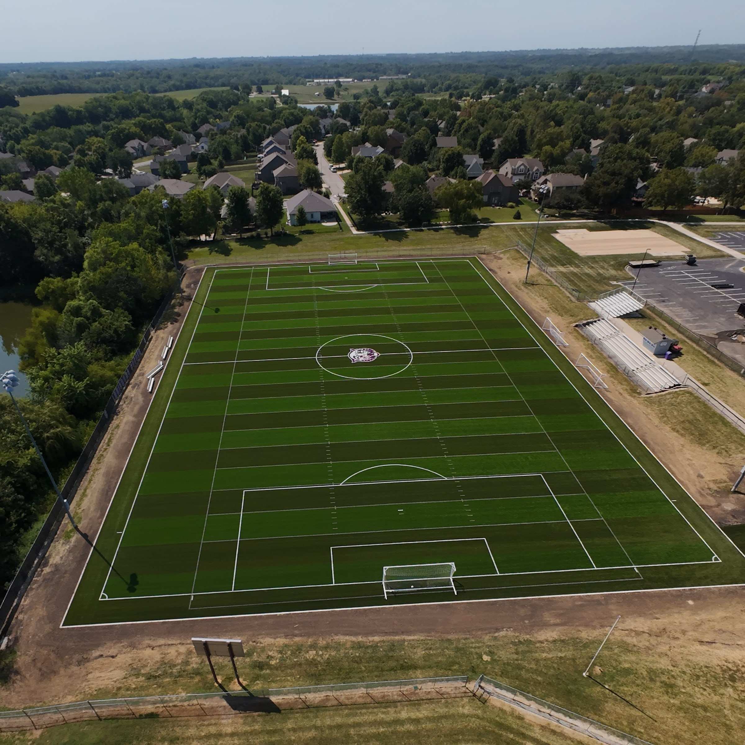 Aerial view of a turf soccer field with goals, bleachers and nearby homes